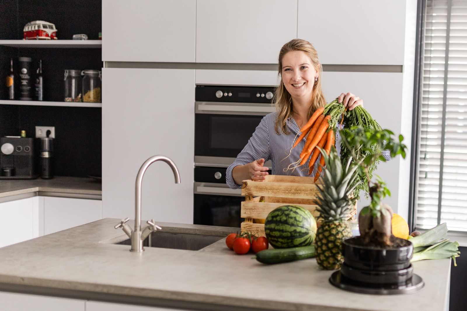 Wendy Reijnders in de keuken met een bos wortels, een kist groenten en fruit